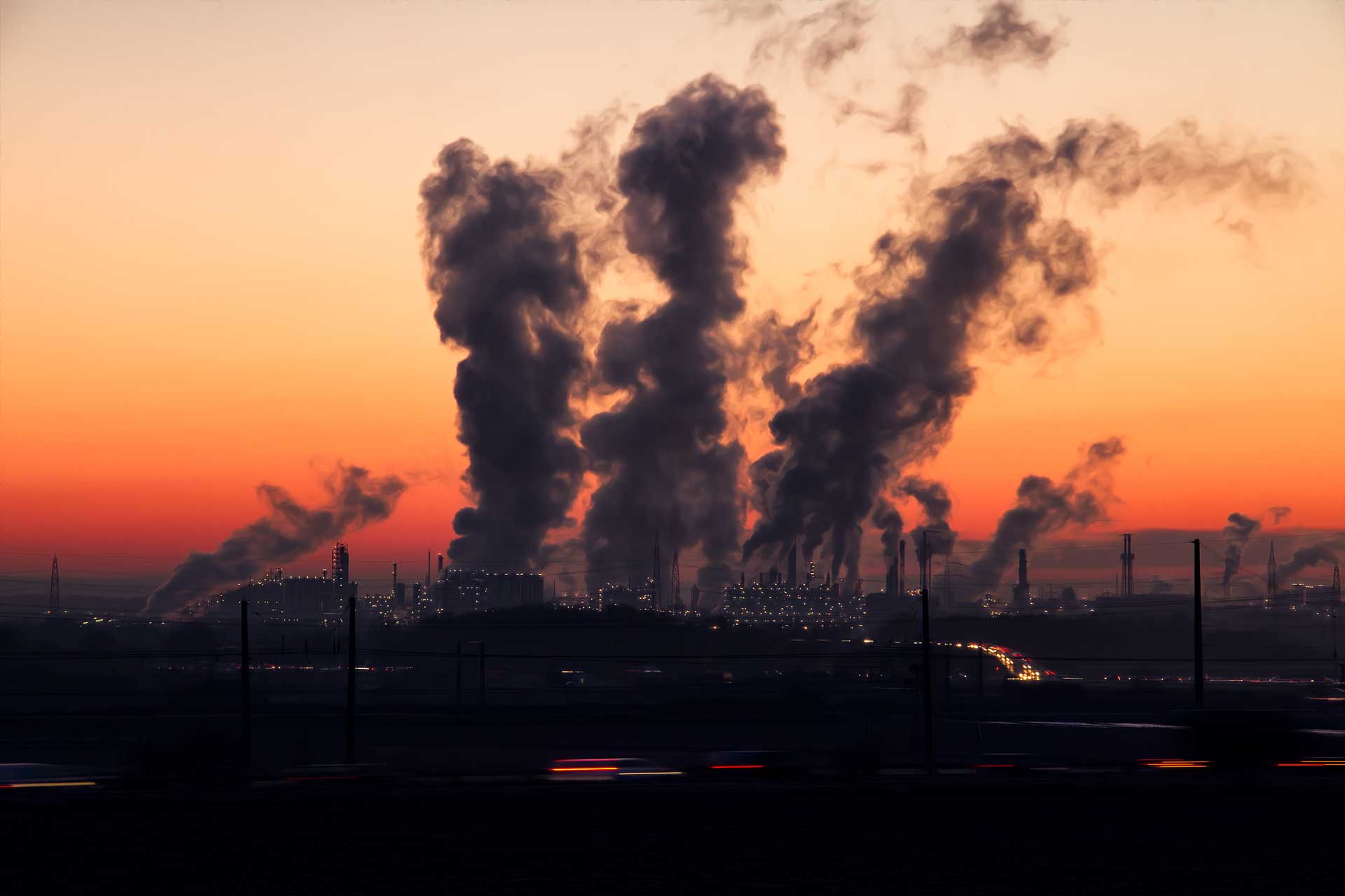 skyline of an industrial area at dusk, with pollution billowing into the sky. 