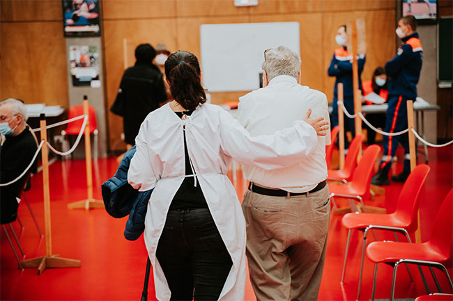 nurse walking with an old man in a vaccine clinic. 