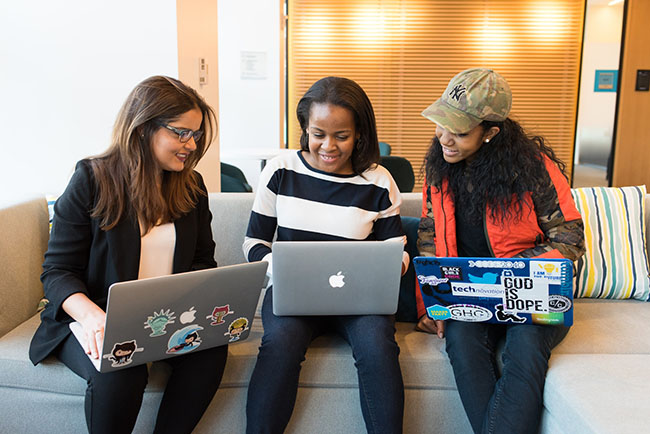 Three women sitting on sofa with laptop