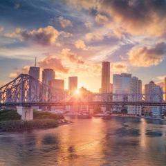 Brisbane city skyline at dusk with sun setting over Story Bridge.