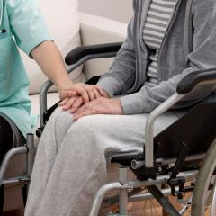 This is an image of a person in medical scrubs holding the hand of another person in a wheelchair
