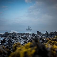 An isolated oil rig at sea off a rocky coastline