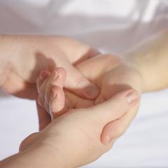 holding hands in a bed with white sheets, implying a medical setting