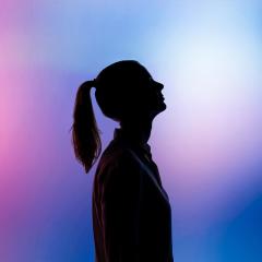 woman in silhouette looking up with a pink and purple background.