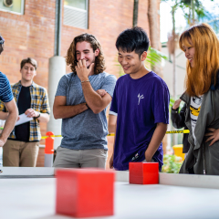 students around a table looking amused by red cubes